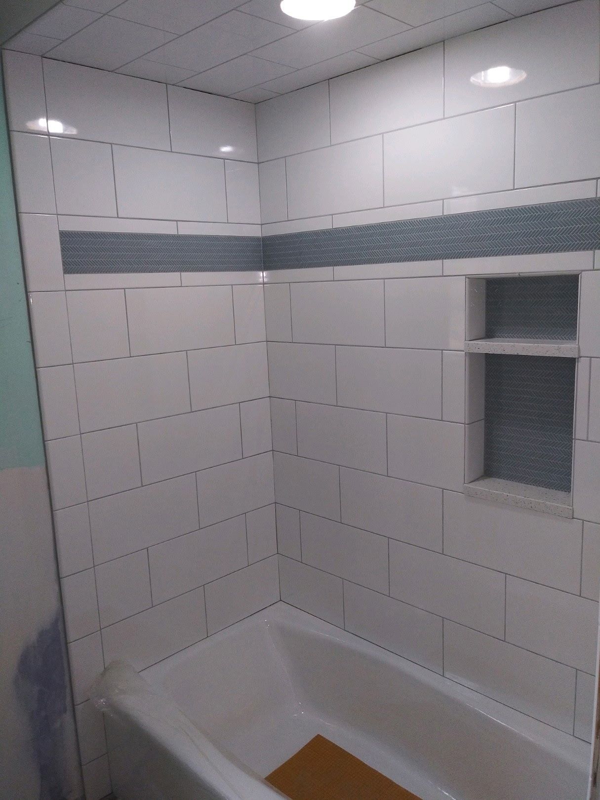 White subway tile shower with a charcoal herringbone accent band and built-in niches