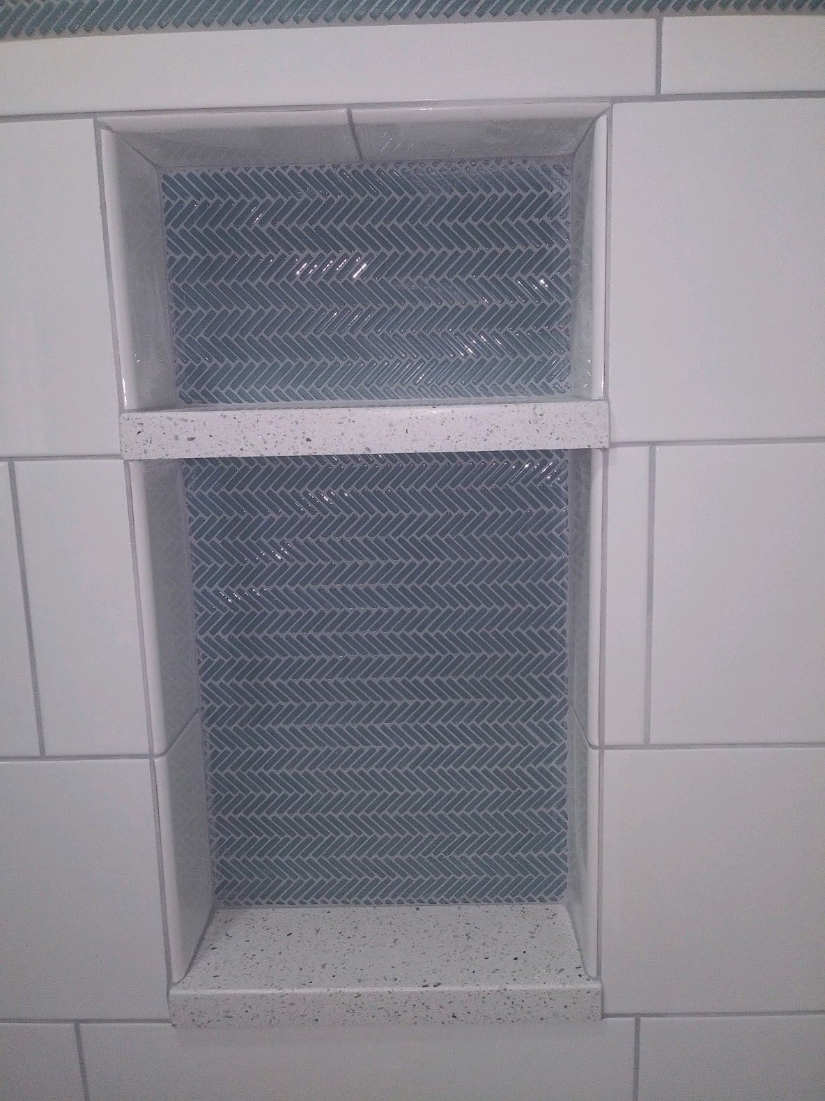 Close view of a recessed shower niche lined with blue-gray herringbone mosaic tile
