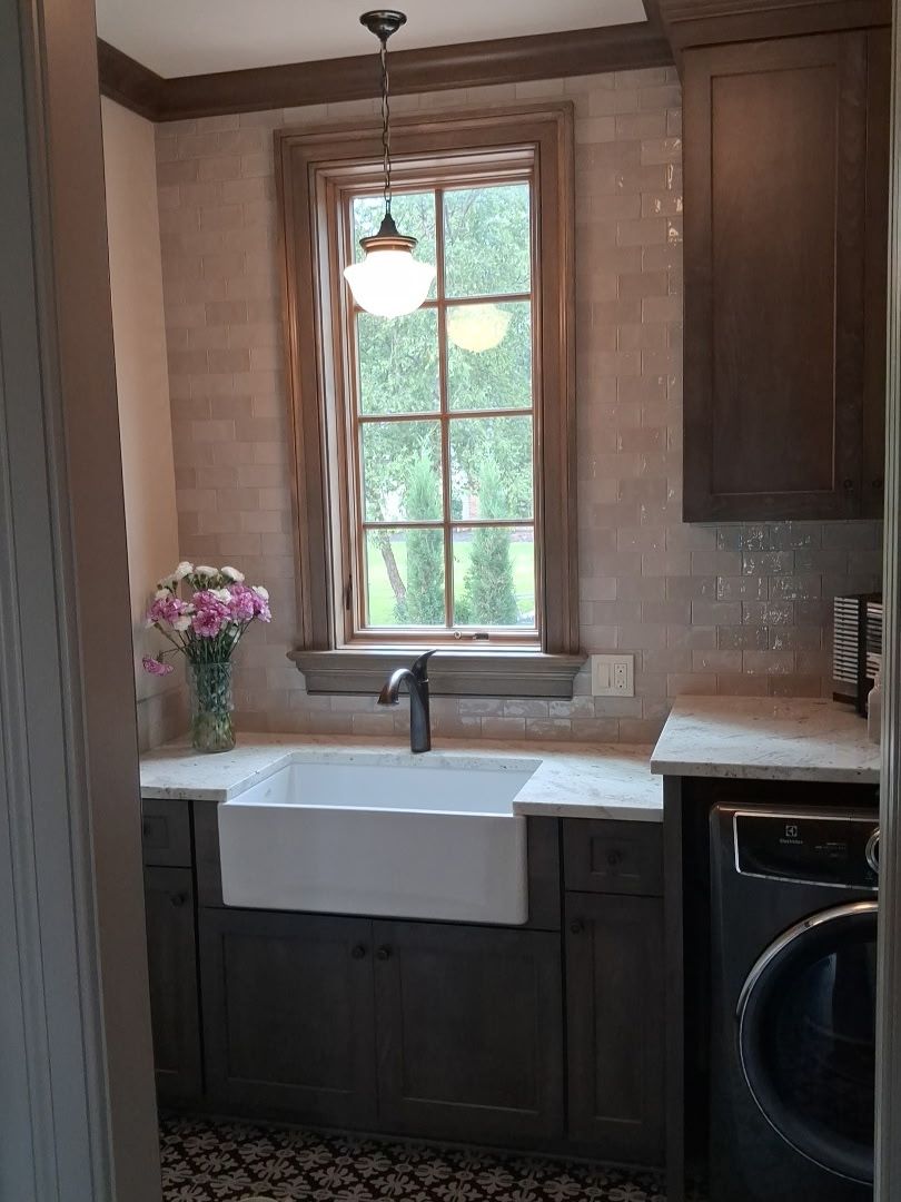 Warm white tile backsplash behind a farmhouse sink with dark cabinetry and a window