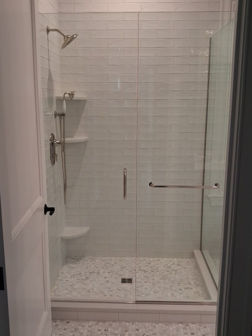 Bright walk-in shower with white stacked tile, glass doors, and polished metal fixtures