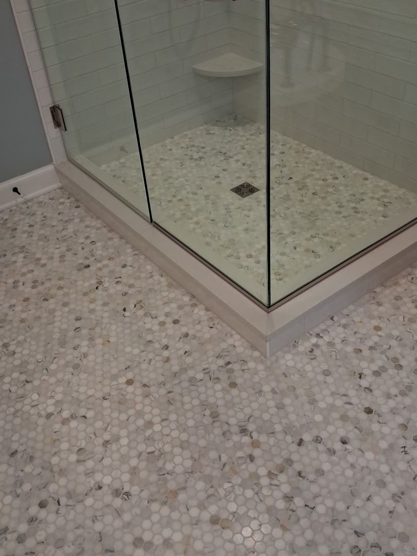 Pebble mosaic tile floor extending into a frameless glass corner shower