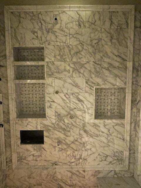 Veined marble shower wall with three mosaic-lined niches and a framed border