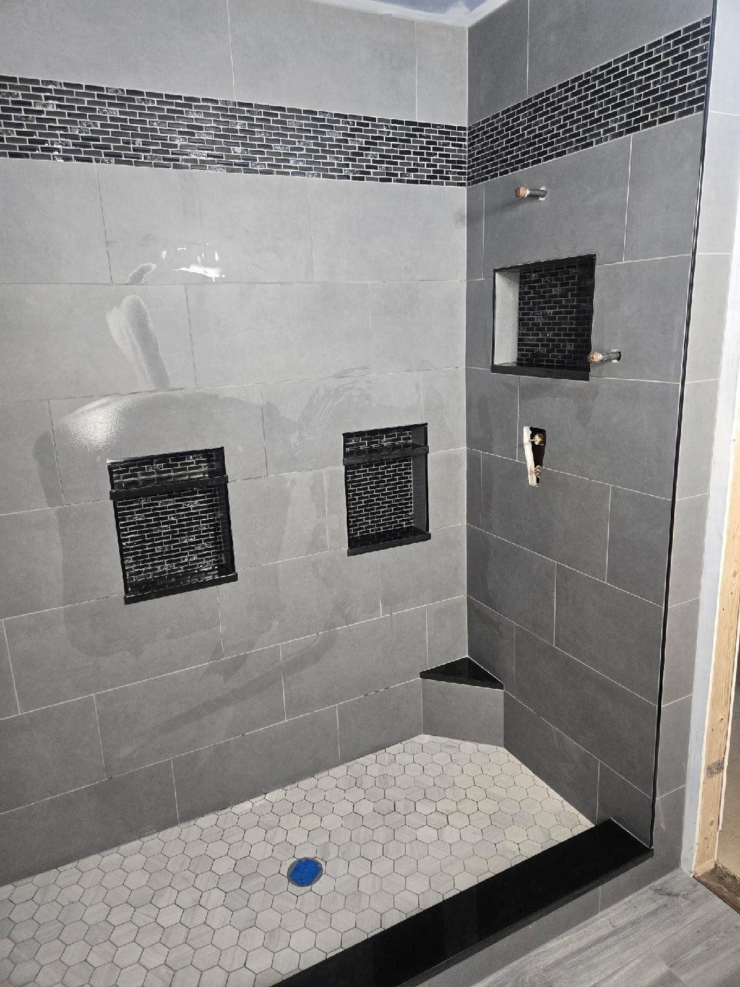 Large-format gray shower tile with black mosaic niches and a hexagon floor